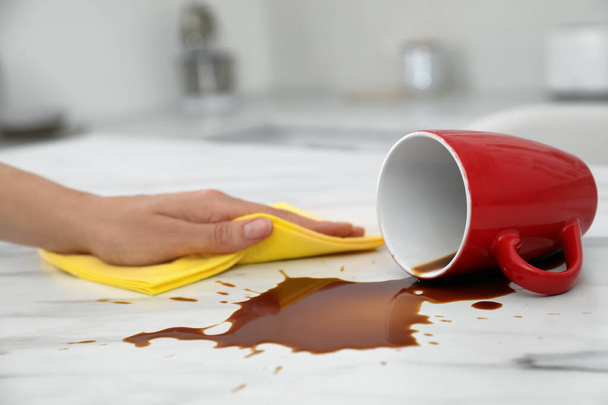 Woman cleaning spilled coffee on white marble table in kitchen, closeup - Foto, Imagem