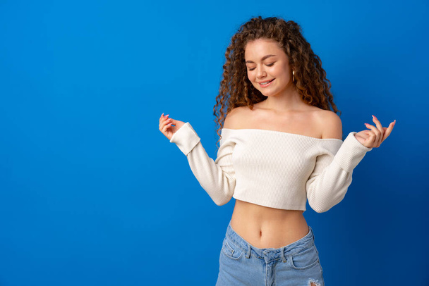 Portrait of a young attractive curly-haired woman against blue background - 写真・画像