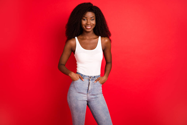 Photo of young attractive afro girl happy positive smile hands in pocket confident isolated over red color background - Zdjęcie, obraz