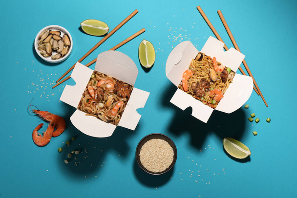 Boxes of wok noodles with seafood and chopsticks on turquoise background, flat lay - Fotoğraf, Görsel