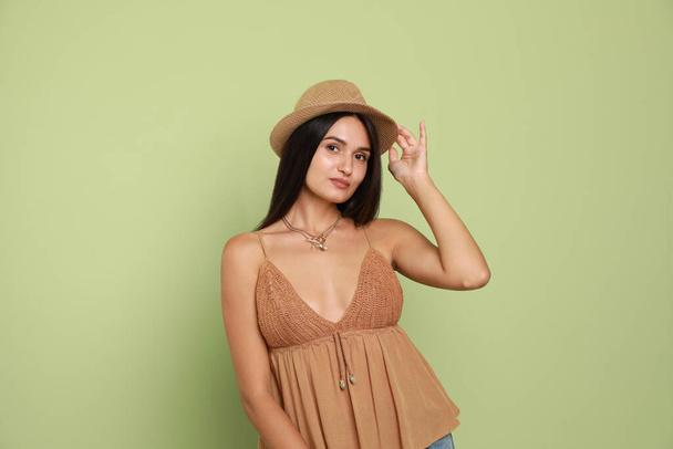 Beautiful young woman with straw hat on light green background - Fotó, kép