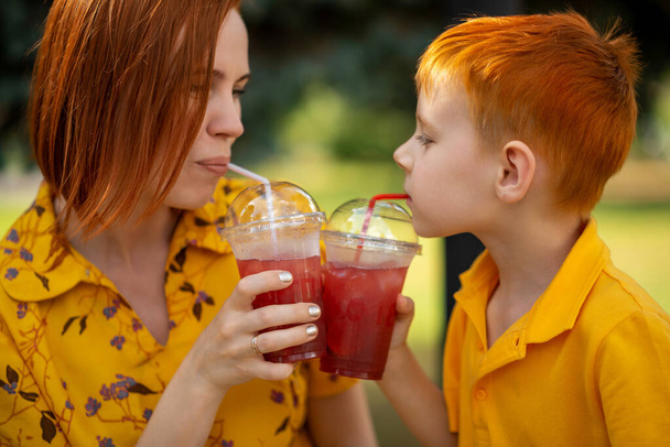 Red-haired young boy and mom are drinking red lemonade. Summer outdoor recreation. - Fotó, kép