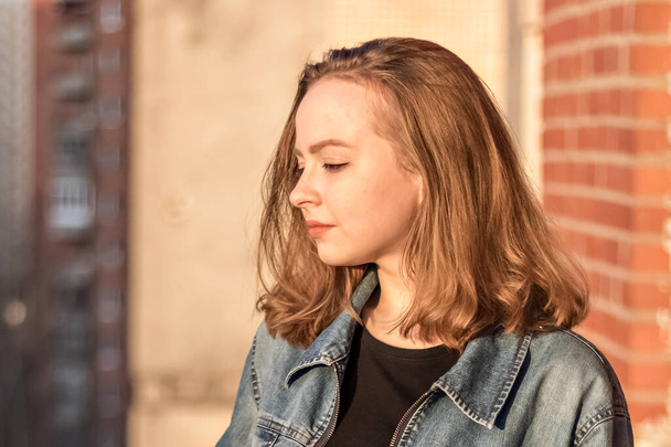 Porträt eines jungen Mädchens im Teenageralter vor einer Ziegelmauer bei Sonnenuntergang. - Foto, Bild