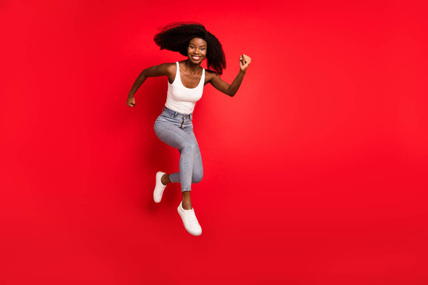 Pleine longueur profil côté photo de jeune afro fille heureux sourire positif sauter vers le haut aller marcher courir presser vente isolé sur fond de couleur rouge - Photo, image