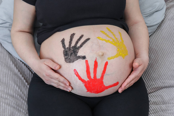 Mujer embarazada sosteniendo su vientre con las huellas de las manos del bebé Bandera belga, vista superior de cerca. - Foto, Imagen