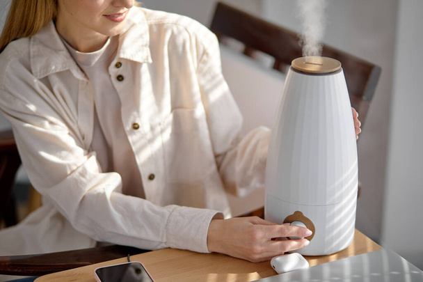 Female turn on aroma oil diffuser on the table at home, steam from humidifier - Foto, Imagem