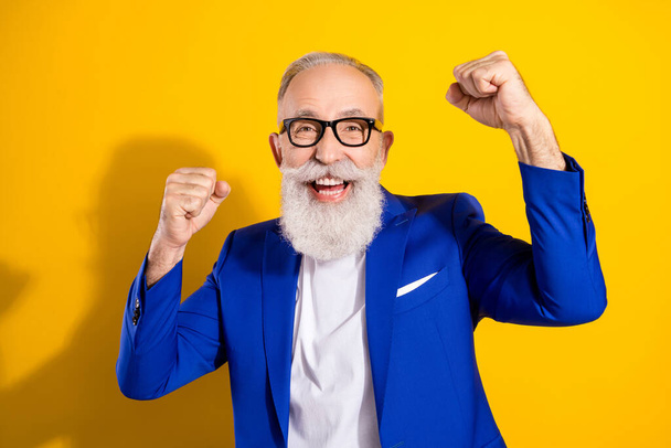 Photo of charming amazed happy old grandfather raise fists winner wear glasses isolated on yellow color background - Zdjęcie, obraz