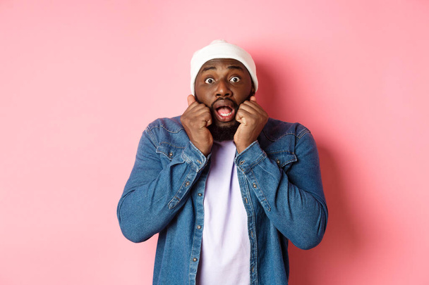 Scared and startled Black man gasping, staring at camera with hands near face, standing shocked over pink background - Photo, Image