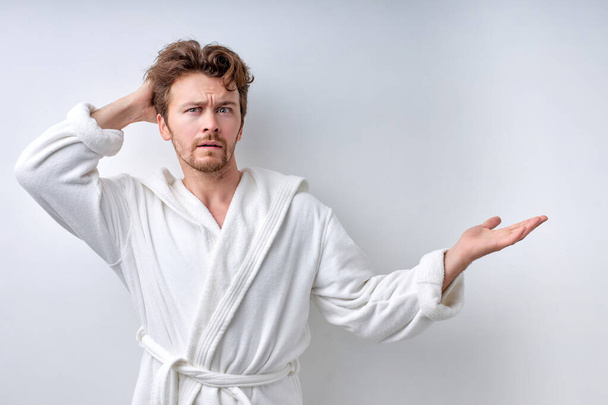 Doubting dissatisfied man at a loss, misunderstanding guy in bathrobe isolated on white - Foto, imagen