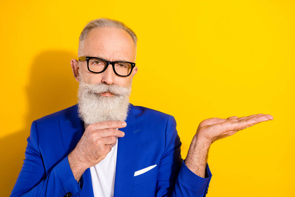 Photo of strict grey beard mature man hold empty space wear spectacles blue jacket isolated on vivid yellow color background - Fotó, kép