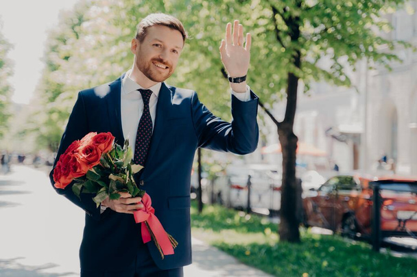 Hombre feliz hombre de negocios en traje con ramo de saludar a alguien en el parque de la ciudad - Foto, Imagen