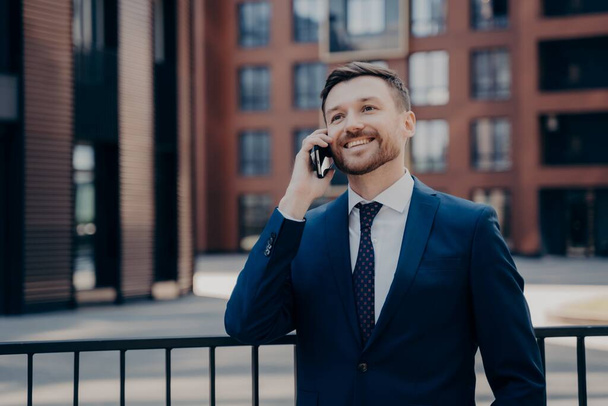 Uomo impiegato godendo piacevole parlare al telefono mentre in piedi accanto a edificio per uffici all'aperto - Foto, immagini