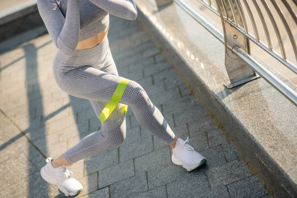 Female sportsperson in grey sportswear exercising with a resistance band - Фото, зображення