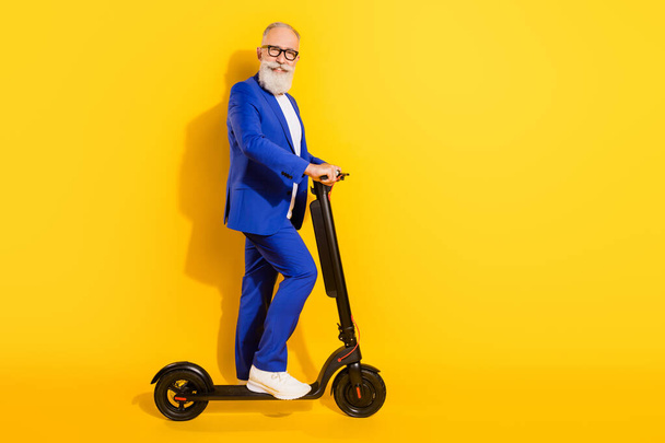 Full size photo of happy smiling good mood mature businessman riding eco scooter isolated on yellow color background - Fotoğraf, Görsel