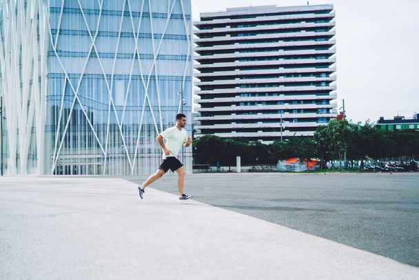 Side view of male athlete jogging with endurance enjoying morning training at city street for running, strong man in sportswear have cardio workout training during leisure for intensive practice - Fotoğraf, Görsel