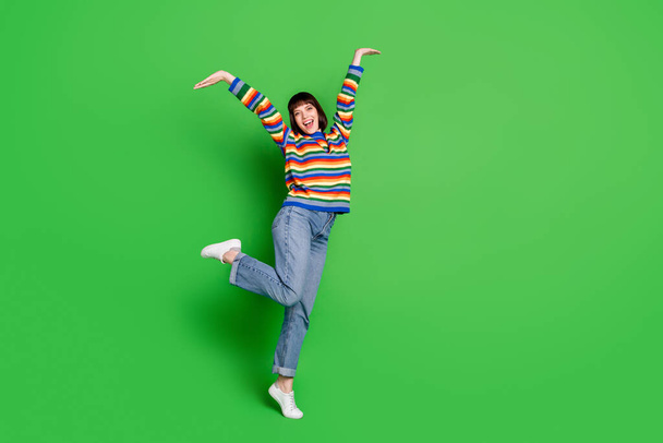 Full length photo of adorable cute young woman wear striped sweater smiling dancing isolated green color background - 写真・画像