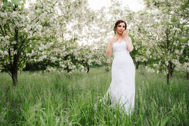 bride in a white dress with a large spring bouquet in a green forest - Фото, изображение