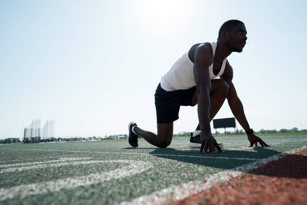 Fotoğraf aşağıda. Afrikalı Amerikalı atlet yarışın başında duruyor. Etkin spor konsepti - Fotoğraf, Görsel