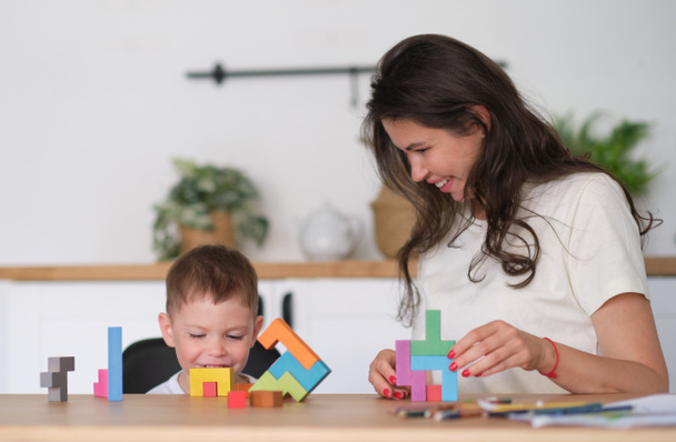 Junge und Mutter spielen zu Hause am Tisch Lernspielzeug. Kinder spielen mit bunten Holzsteinen am Tisch. - Foto, Bild