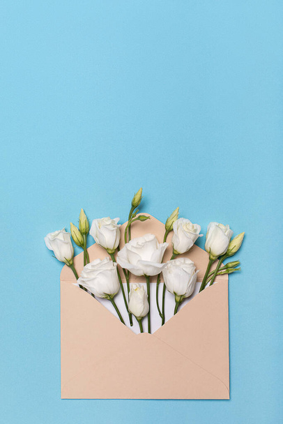 Verticale shot bloem knop plat lag in een envelop lisianthus of eustoma, texas bel en prairie gentiaan, Ierse roos, op pastel blauwe achtergrond met kopieerruimte. Concept voor wenskaart. - Foto, afbeelding