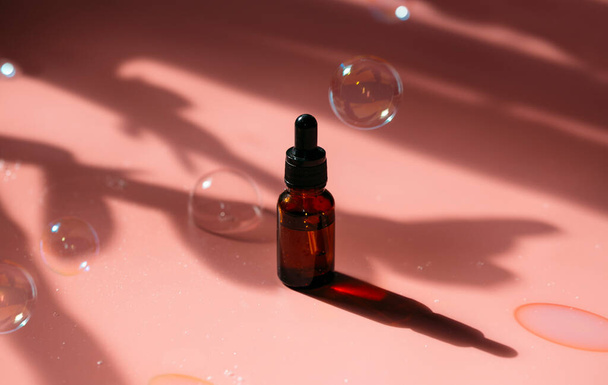 botella de aceite esencial de vidrio sobre fondo rosa con burbujas de jabón volador - Foto, imagen