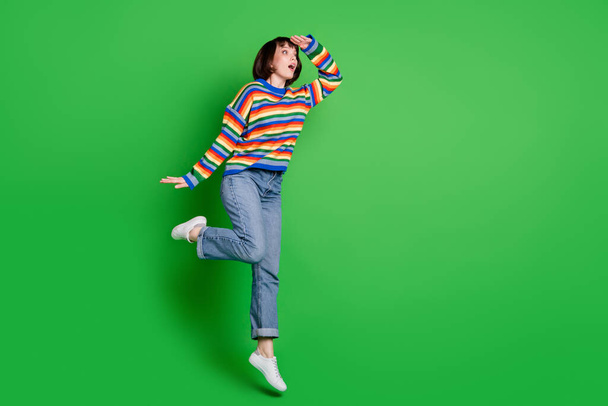 Full length photo excited shiny lady dressed pullover jumping high arm forehead looking far empty space isolated green color background - Fotografie, Obrázek