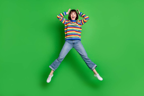Full length photo adorable impressed lady dressed colorful pullover jumping high arms head smiling isolated green color background - Фото, зображення