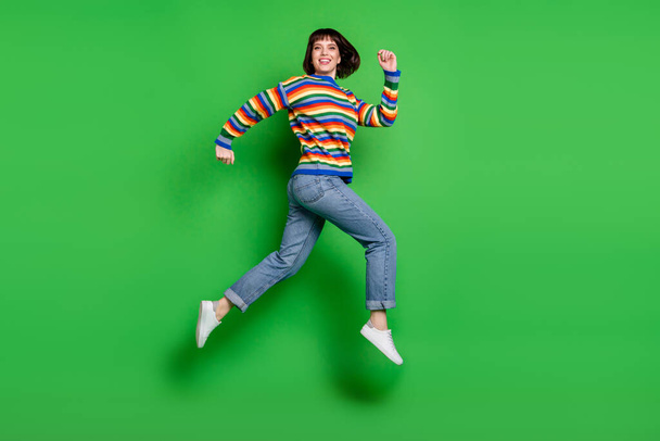 Full length photo funny cute young lady dressed colorful pullover jumping running smiling isolated green color background - Foto, imagen