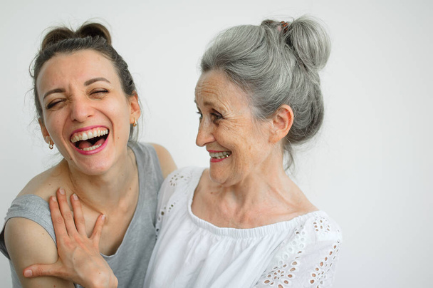Šťastná starší matka objímá svou dospělou dceru, ženy se spolu smějí, upřímná rodina různých věkových generací se baví na bílém pozadí, Den matek. - Fotografie, Obrázek