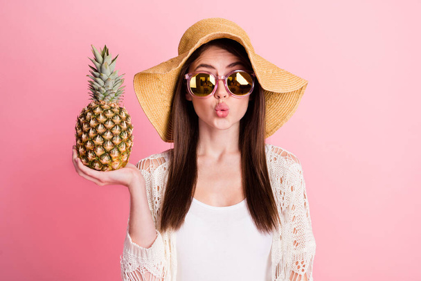 Photo of adorable lady hand palm hold pineapple kiss lips wear cap isolated on pink color background - Fotó, kép