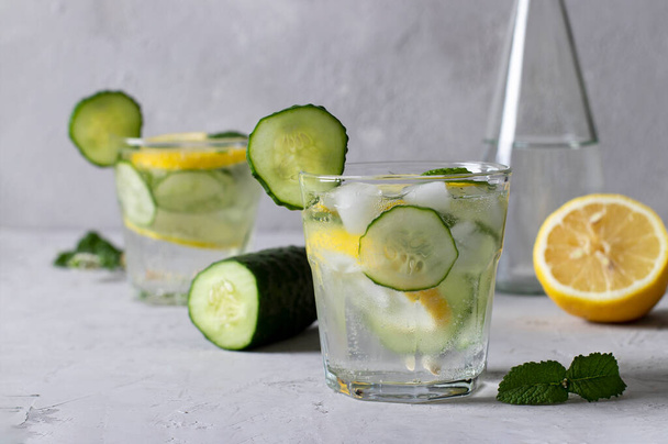 Two summer fresh ice drinks with mint, lemon and cucumber, plus a bottle of mineral water. Healthy mojito detox cocktail on light gray background. - Foto, Bild