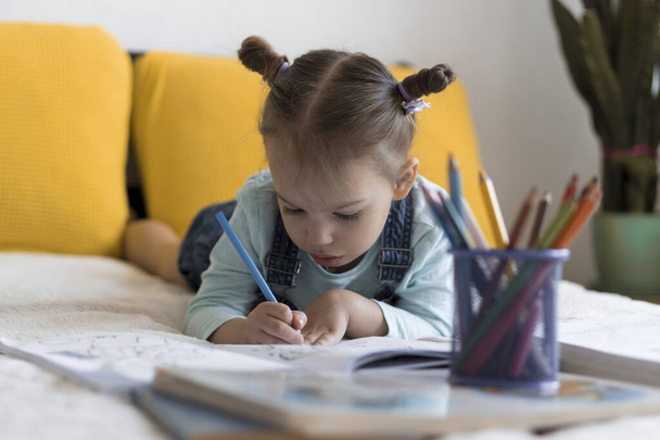 Zeki, gülümseyen, küçük bir çocuk çocuk ve kız sarı yatakta göbeklerinde kalemlerle resim yapıyorlar. Küçük sevimli okuyucu evde karantinada eğleniyor, mutlu çocuk. Arkadaşlık, aile, eğitim. - Fotoğraf, Görsel