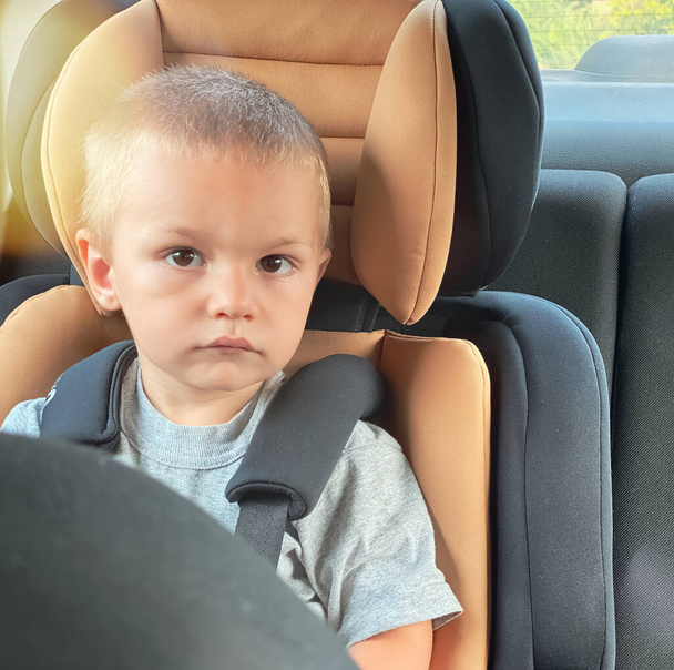 Niño caucásico en un asiento de coche negro con un centro de melocotón. - Foto, Imagen