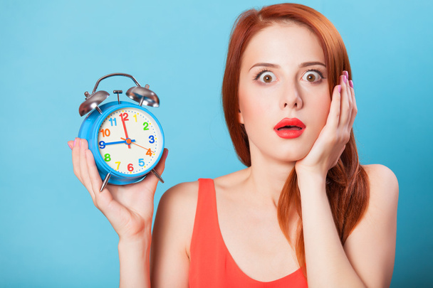 Surprised redhead women woth alarm clock on blue background. - Photo, Image