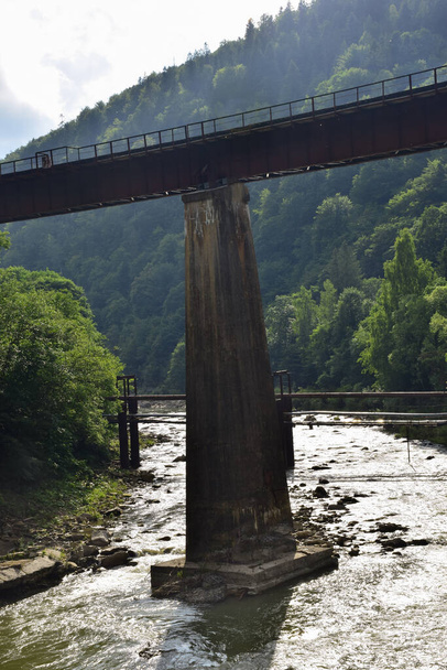 Above the turbulent mountain river, a pedestrian bridge with railings rises on long concrete columns. Photographed in the summer, no people - Photo, Image