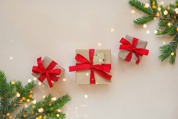 Χριστούγεννα και Πρωτοχρονιά διακοπές φόντο. Χριστουγεννιάτικα κλαδιά δέντρου, τρία κουτιά δώρου με κόκκινα τόξα σε μπεζ φόντο. Πάνω άποψη, επίπεδη lay, αντίγραφο χώρου. - Φωτογραφία, εικόνα
