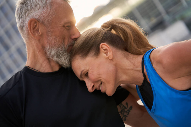 Retrato de pareja afectuosa de mediana edad, hombre y mujer en ropa deportiva haciendo ejercicio matutino en la ciudad en un día de verano - Foto, imagen