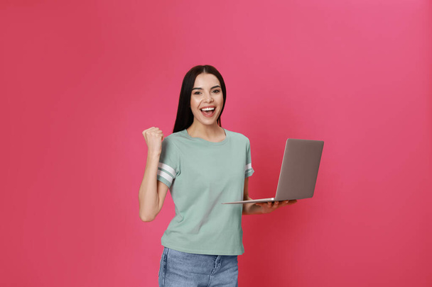 Emotional young woman with modern laptop on pink background - Photo, image