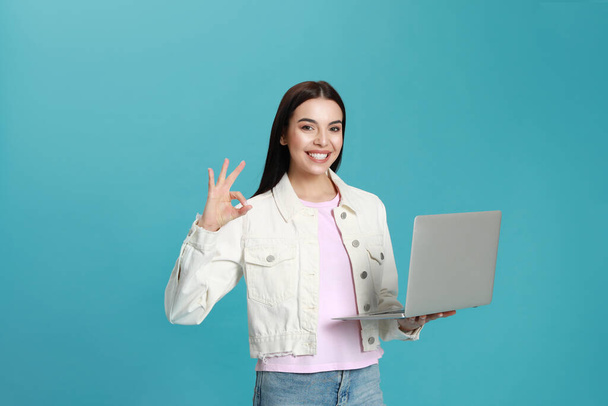 Young woman with modern laptop on light blue background - Foto, afbeelding