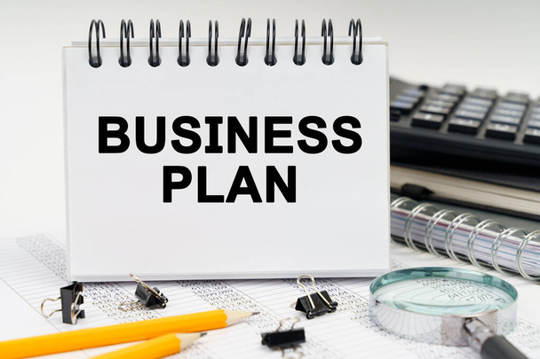 Business and economy concept. On the table is a magnifying glass, pencils, diaries and a notebook with the inscription - BUSINESS PLAN - Fotó, kép