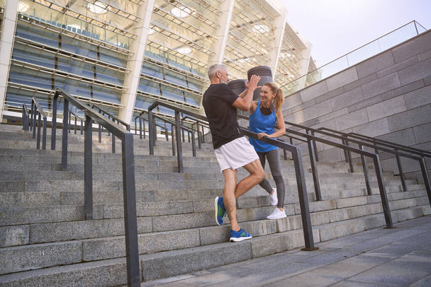 Deportiva pareja de mediana edad dando unos a otros cinco altos después de hacer ejercicio juntos al aire libre - Foto, imagen