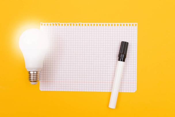 A Power Saving Lamp with Notepad Lying on Yellow Table - 写真・画像