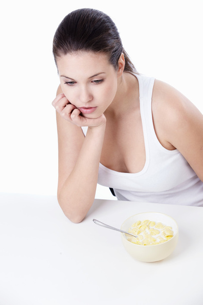 Chica pensativa con un tazón de hojuelas de maíz sobre un fondo blanco
 - Foto, imagen