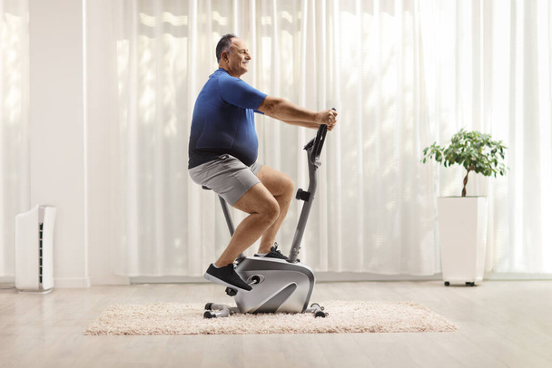 Full length profile shot of a mature man riding a stationary bike at home - Photo, image