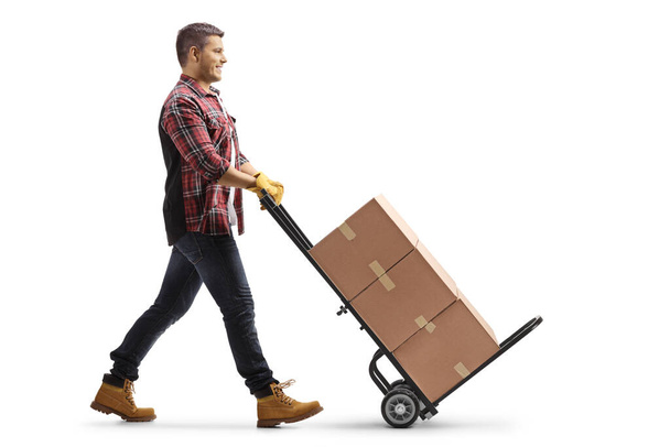 Full length profile shot of a man pushing a hand truck with cardboard boxes isolated on white background - Фото, зображення