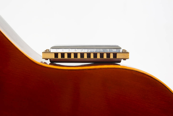 The harmonica rests on the body of a classical guitar. Classical musical wind instrument - Photo, Image