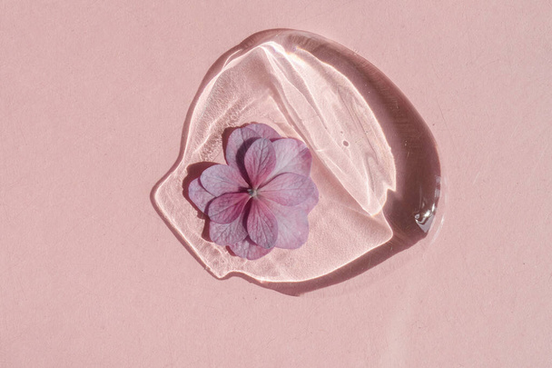 A drop of transparent cosmetic gel with flower on a pink background. - Photo, image