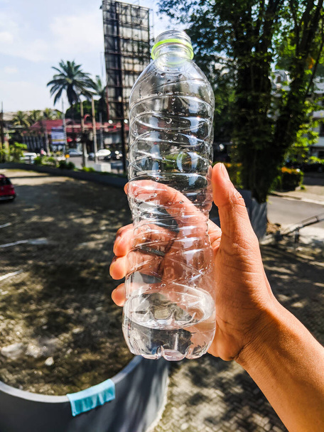 ruka držící láhev s pitnou vodou, která má jen malé množství vody - Fotografie, Obrázek