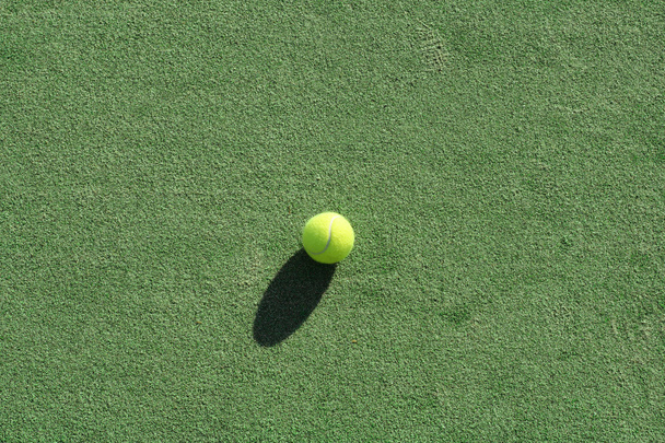 Tennis ball on a green artificial court surface,natural lighting and shadows. - Fotoğraf, Görsel