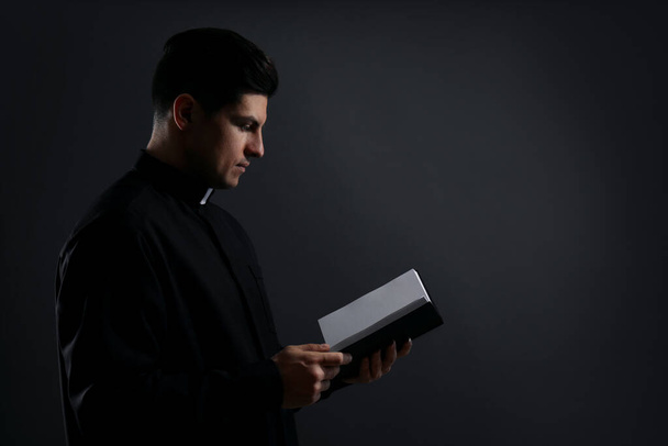 Priester mit Bibel auf schwarzem Hintergrund. Raum für Text - Foto, Bild